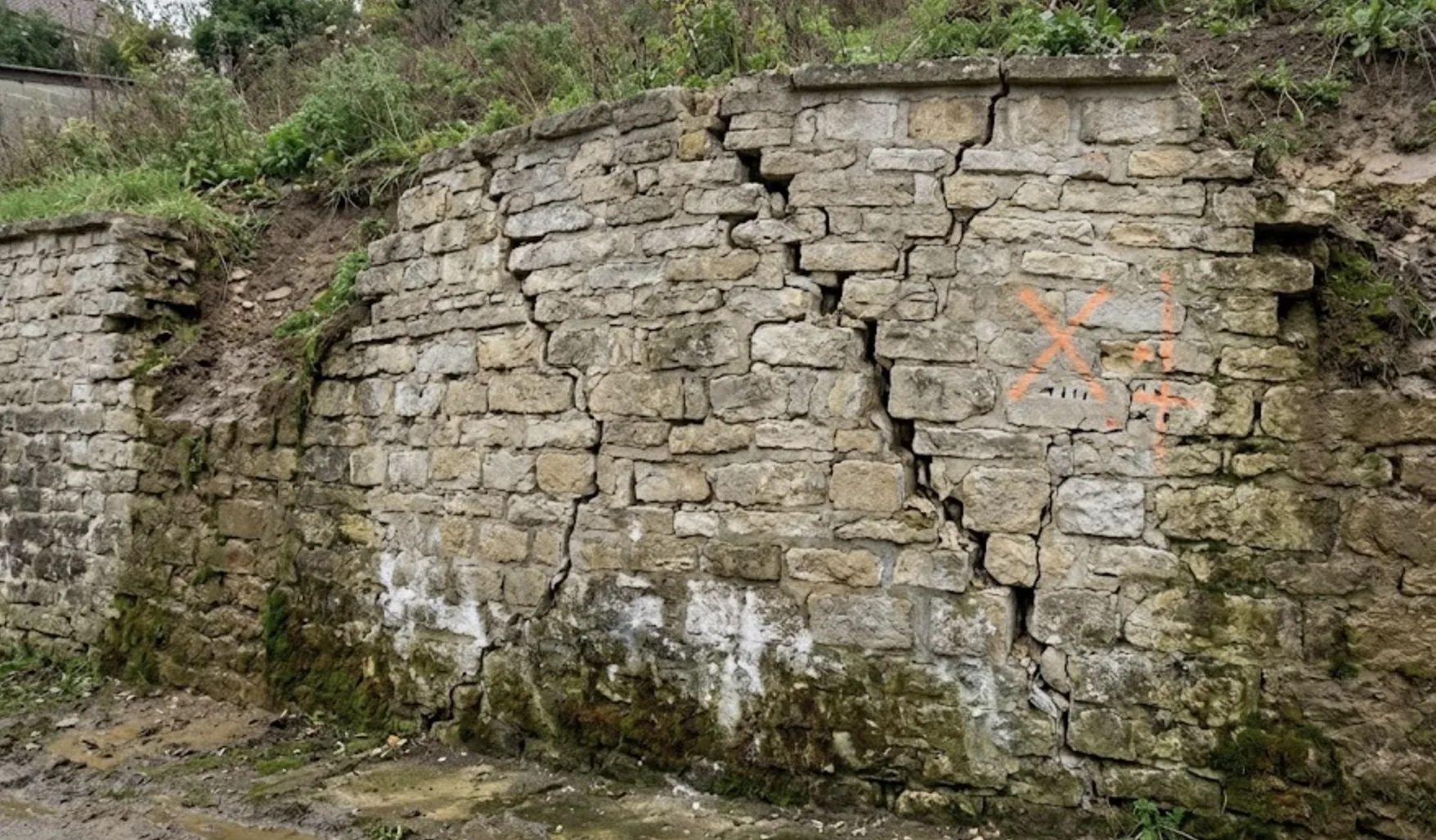Mur de soutènement en pierre présentant un ventre de bœuf et des fissures, risque d'effondrement
